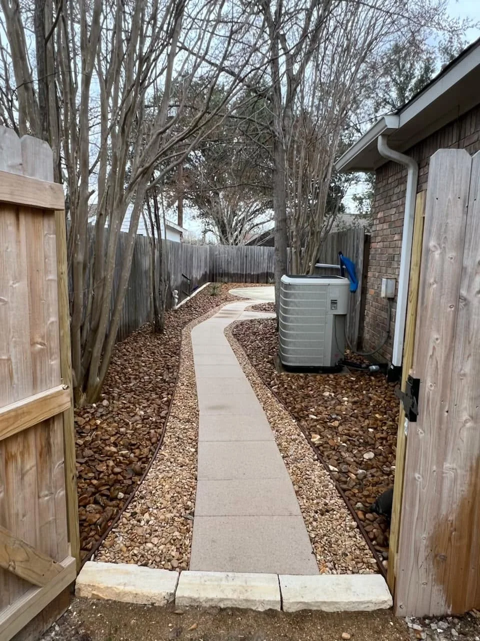 Stone path through gravel along a side yard between a house and cedar fence