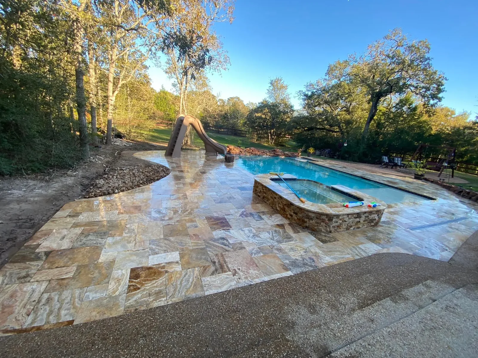 Travertine pool deck and coping installed around a backyard pool in Bryan, Texas